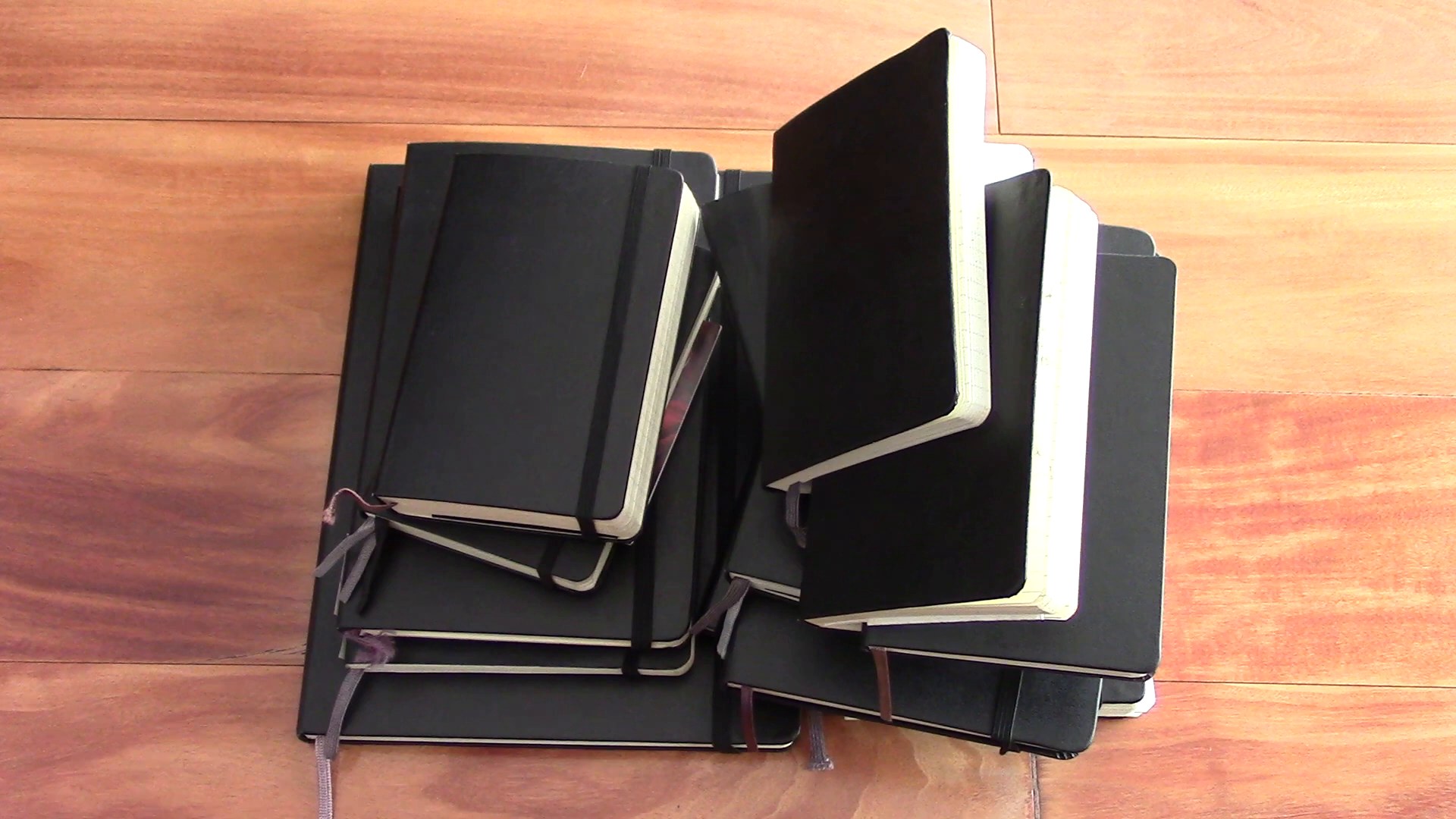 Large collection of old Moleskine notebooks stacked on a wooden desk